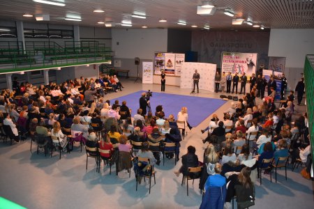 W hali sportowej trwa spotkanie inauguracyjne. Na krzesłach ustawionych w kształcie litery U siedzą panie, które zapisały się na kurs. Pośrodku mata do ćwiczeń. Z tej strony, na której nie ustawiono krzeseł stoją organizatorzy kursu. Za ich plecami ścianki reklamowe i baner zachęcający do udziału w kursie samoobrony