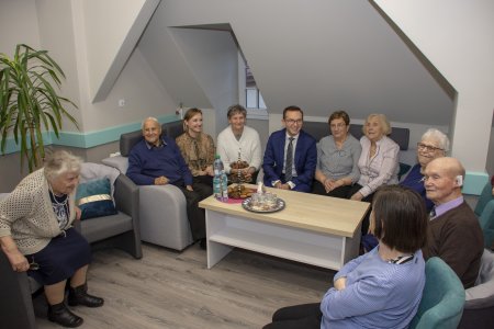 Momieszczenie na poddaszu. Ma pięknie uformowany sufit z wieloma załamianiami. W pokoju wokół małego stolika siedzi grupa seniorów i jako gość - prezydent Ciechanowa