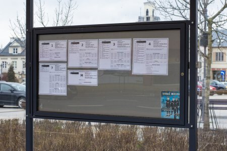 Tablica informacyjna ustawiona na przystanku komunikacji miejskiej, na której zawieszono nowe, powiększone rozkłady jazdy 