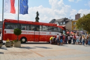 Na placu Jana Pawła II stoi oznakowany autokar - mobilny punkt  poboru krwi. Przed przednimi drzwiami autokaru stoi kolejka chętnych do oddania krwi. Obok, przy stoliku kolejni chętni wypełniają ankiety