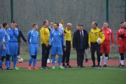 Uczestnicy meczu między urzędnikami i nauczycielami ubrani w sportowe stroje stoją na skraju boiska