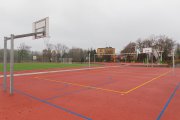 Boisko do koszykówki. Za nim widać plac zabaw dla dzieci