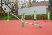 Na pierwszym planie huśtawka, za nią urządzenia do ćwiczeń, tak zwana zewnętrzna siłownia