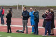 Na skraju boiska, między innymi osobami, stoi K. Kosiński ubrany w sportowy stój. Ludzie biją brawo obserwując mecz między urzędnikami i nauczycielami