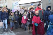 Dzieci niosą transparent z nazwą swojego przedszkola. Dzieciaki idą w papierowych koronach na głowach