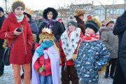 Grupa uczestników orszaku na pl. Jana Pawła II. Na pierwszym planie trójka dzieci w królewskich koronach. Jedno dziecko ma pelerynę zrobioną z jasnej tkaniny przewiązanej na ramionach