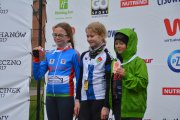 Zbliżenie na 3 uśmiechnięte dziewczynki z medalami na piersiach. Dwie z nich lekko unoszą w górę swoje trofea