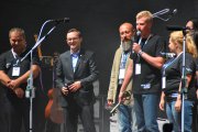 Przedstawiciel studentów z kluczem w ręku mówi do mikrofonu. Obok stoją jego koledzy studenci. Po prawej stoi uśmiechnięty prezydent Ciechanowa i rektor uczelni