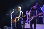 Występ zespołu Happysad. Na pierwszym planie dwóch muzyków z gitarami. Jeden z nich śpiewa do mikrofonu.