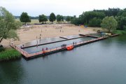 Zdjęcie wykonane z drona. Widać nowy pomost i plażę na kąpielisku Krubin. Na pomoście i plaży są ludzie. Przy pomoście stoi łódka