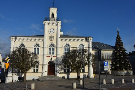 Ciechanowski ratusz przy słonecznej pogodzie. To okres świąteczny, bo po prawej stronie ratusza stoi wysoka choinka. Nad ratuszem błękitne niebo.