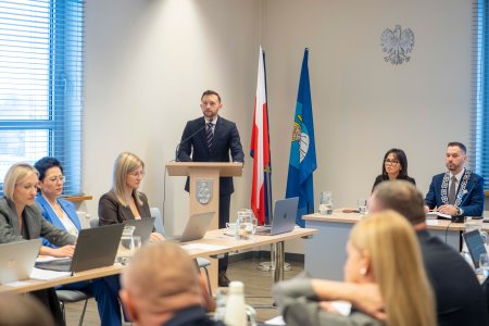Trwa sesja rady miasta. Radni i zastępczynie prezydenta Ciechanowa siedzą za stołami. W centrum fotografii, za mownicą stoi prezydent Ciechanowa Krzysztof Kosiński. Po prawej stronie znajduje się stoł prezydialny z przewodniczącymi rady.